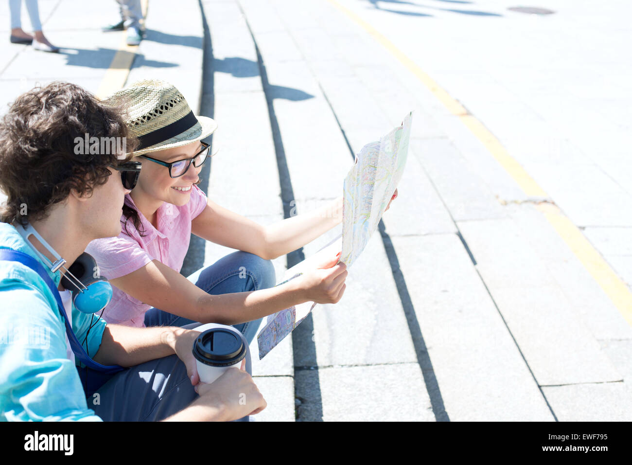 Heureux couple reading map while sitting on steps outdoors Banque D'Images