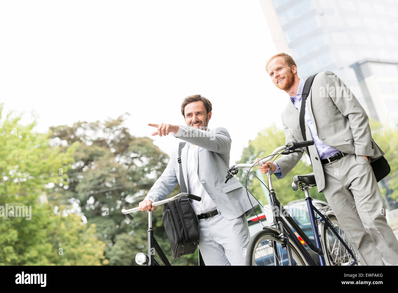 Smiling businessman with bicycle montrant quelque chose à collègue on street Banque D'Images