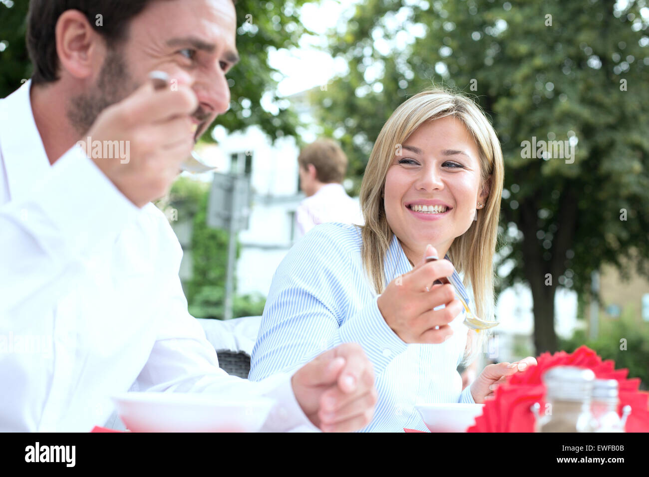 Happy businesswoman manger des aliments avec des collègue at sidewalk cafe Banque D'Images