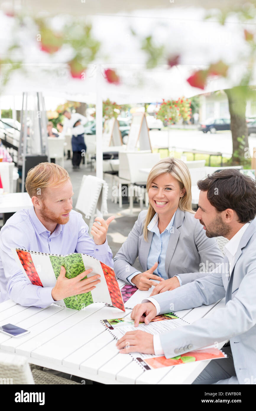 Portrait of happy businesswoman avec collègues masculins menu décider at sidewalk cafe Banque D'Images