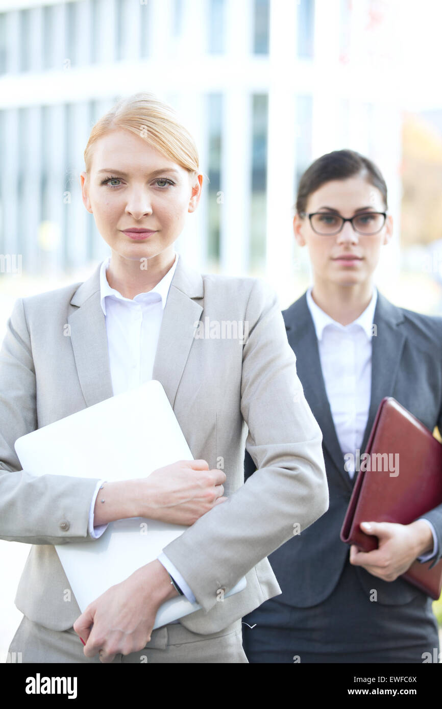 Portrait of businesswoman holding laptop avec collègue en arrière-plan Banque D'Images