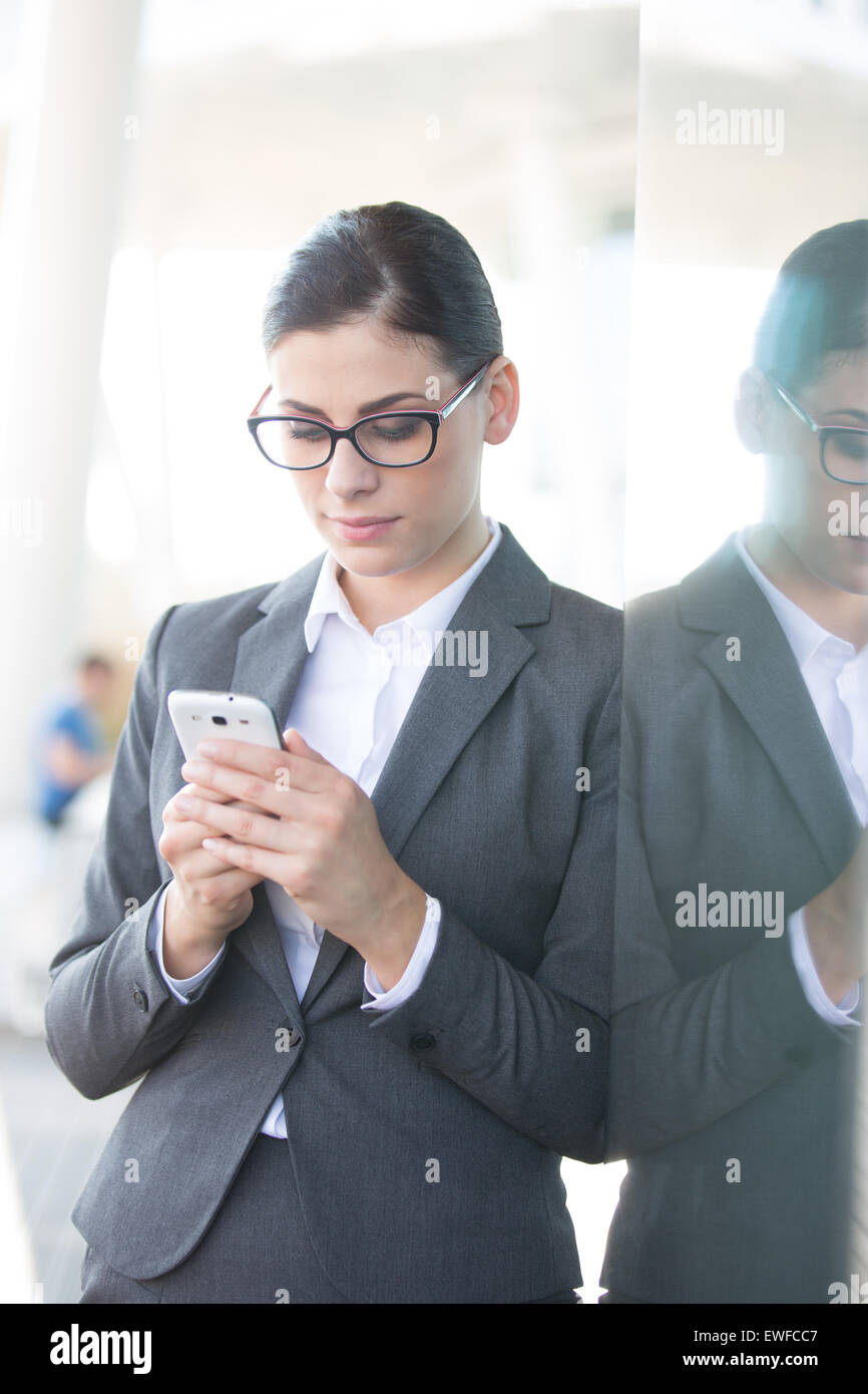 Businesswoman using cell phone tout en s'appuyant sur la paroi de verre Banque D'Images