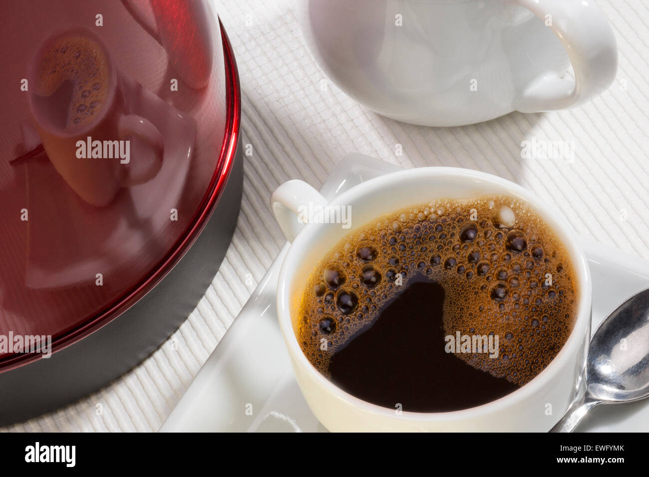 Une tasse de café noir avec un reflet sur le côté d'une bouilloire électrique Banque D'Images