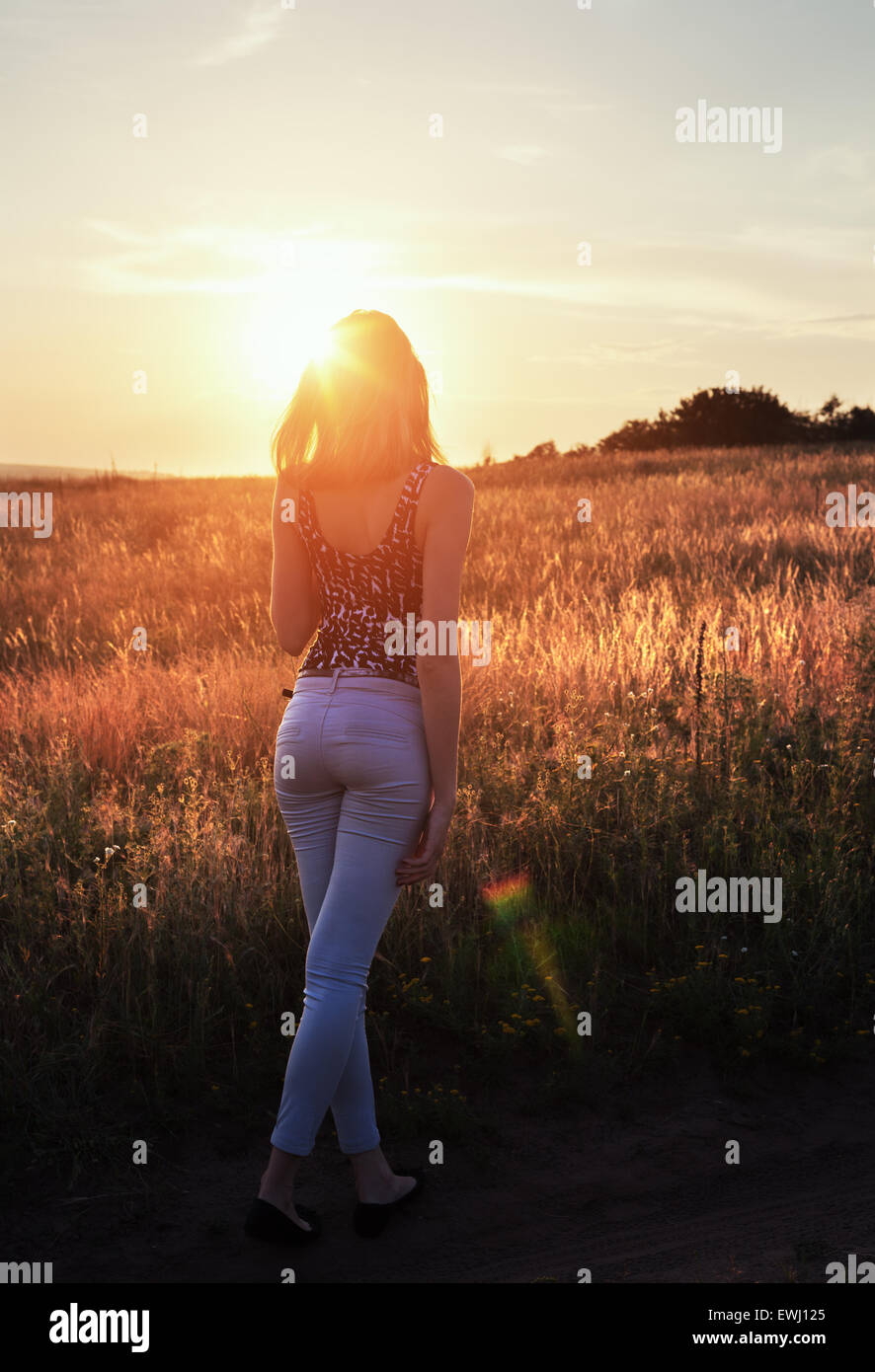 Free happy young woman raising arms au coucher du soleil dans le domaine en été. Contexte Banque D'Images