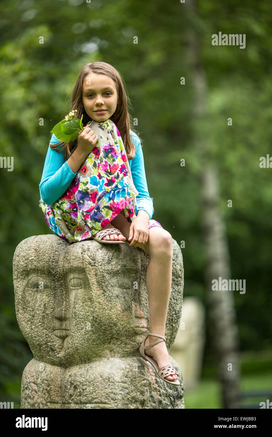 Jolie petite fille assise sur un totem en pierre dans le parc. Banque D'Images