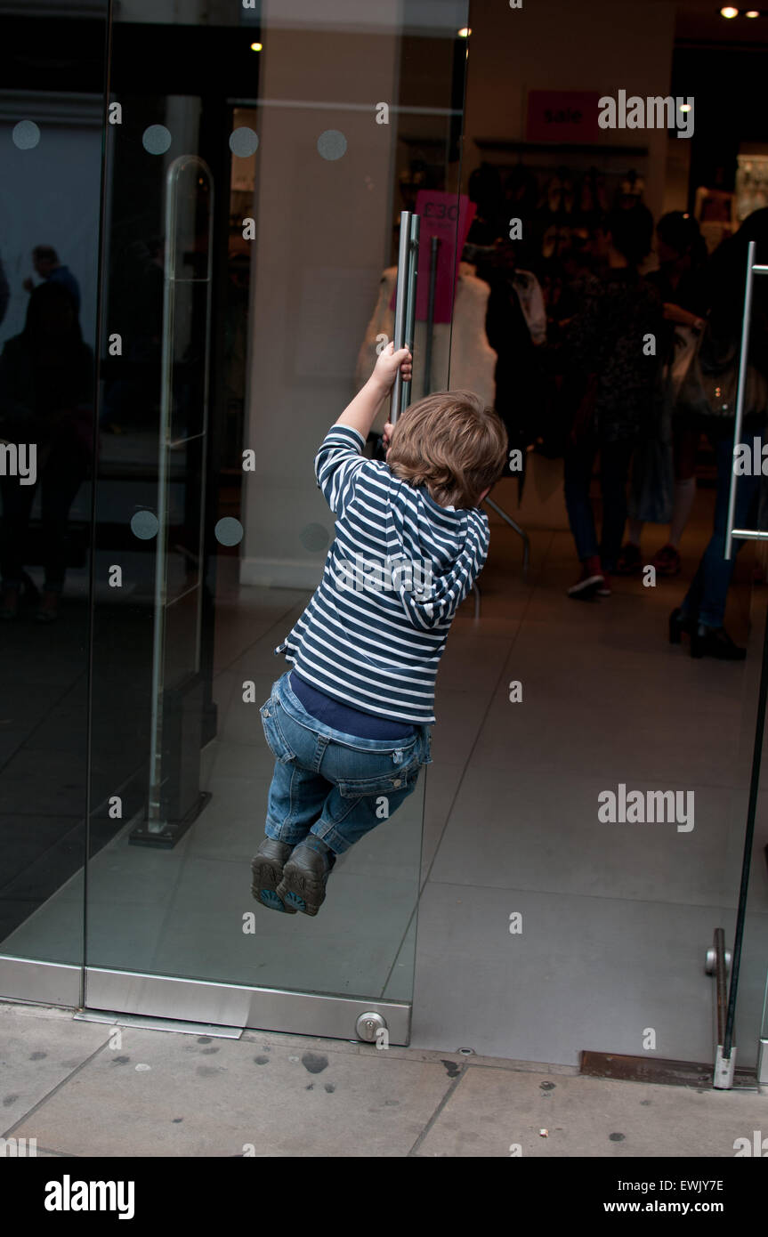 Boy swinging sur une porte de boutique Banque D'Images