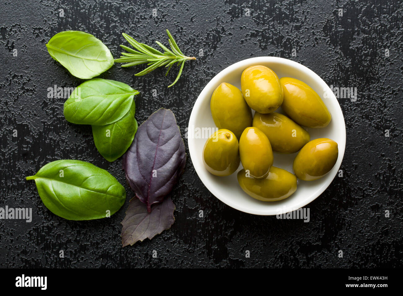 Les olives vertes et les herbes sur tableau noir Banque D'Images