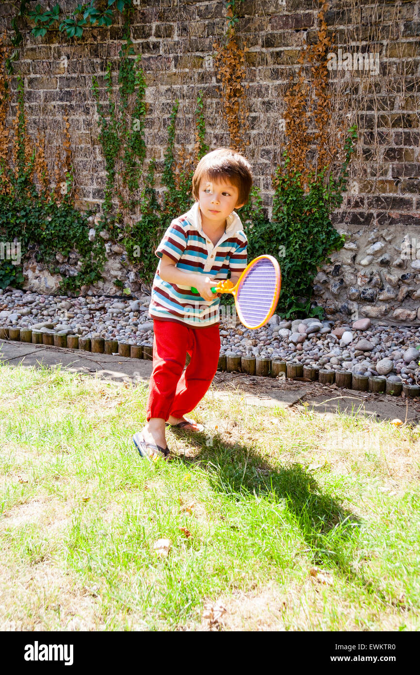 Caucasien enfant, garçon, 4-5 ans, en jardin, vêtus de t-shirt et pantalon,  tenant une raquette de tennis en plastique et la bille à jouer au tennis  sur la pelouse Photo Stock -