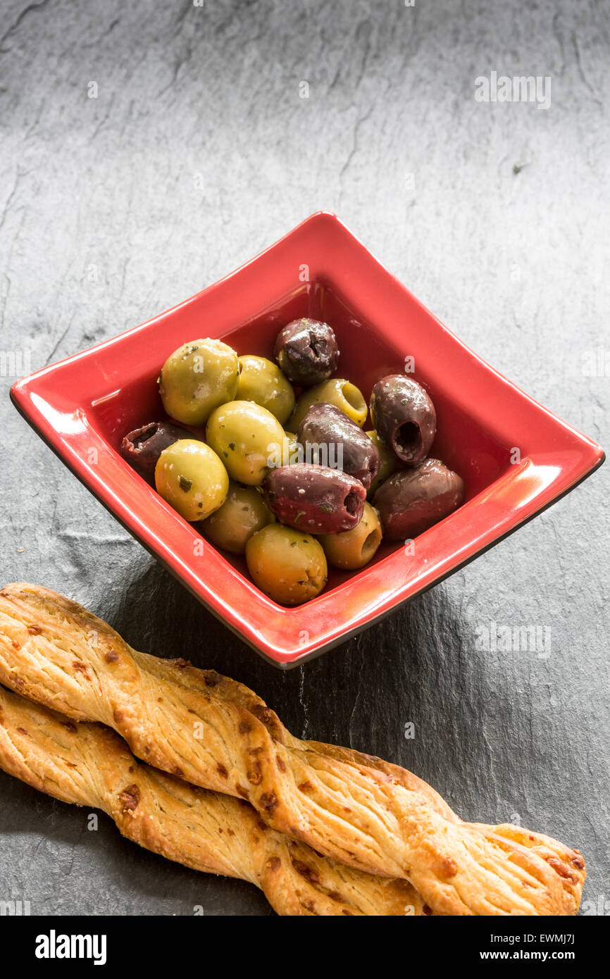 Mixed Olives dans un plat carré rouge avec le fromage de gruyère et de pavot Pain sur ardoise Banque D'Images