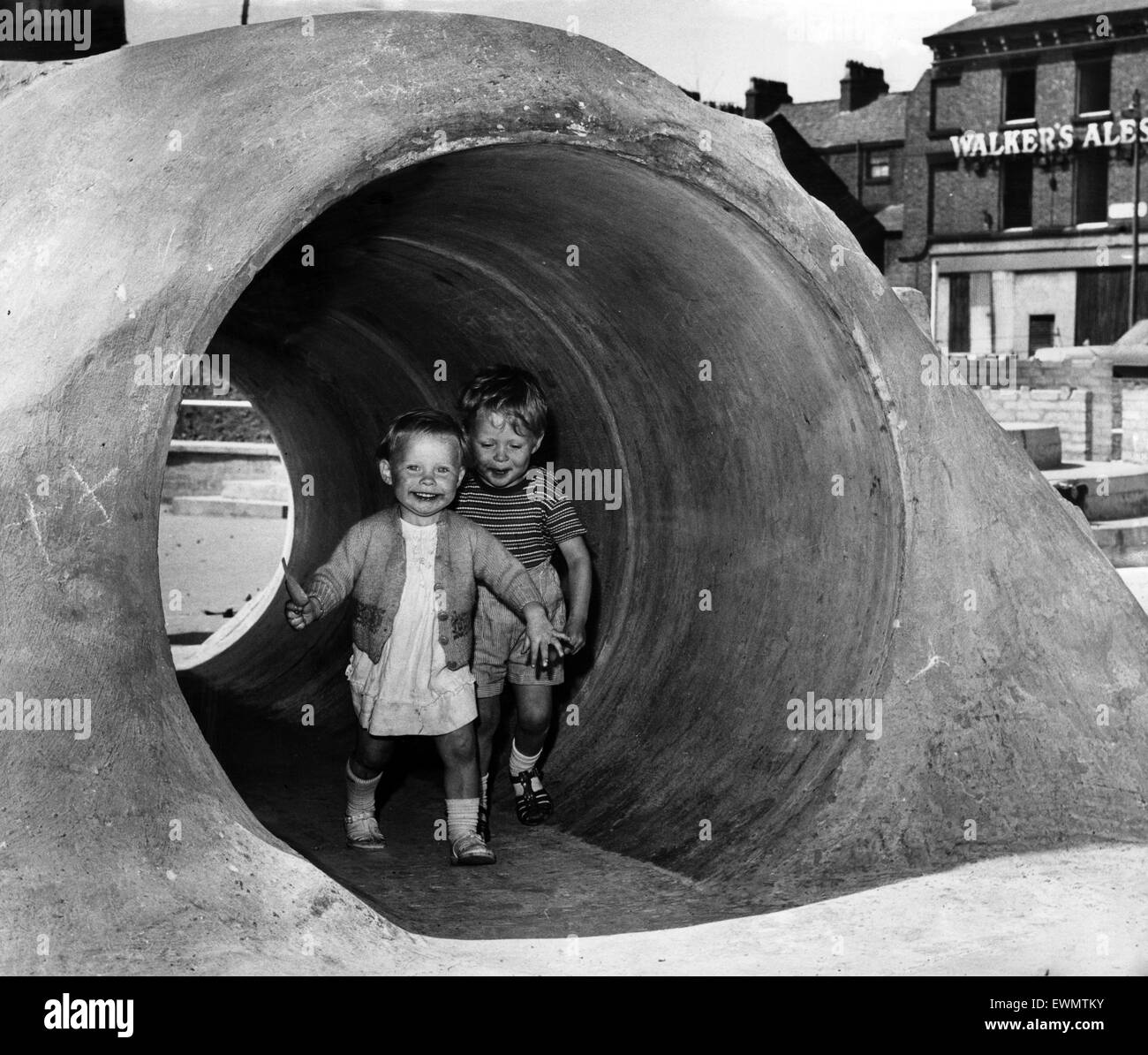Deux jeunes enfants s'amusant qui traverse un tunnel en béton dans une aire de jeux. 2 juin 1966. Banque D'Images