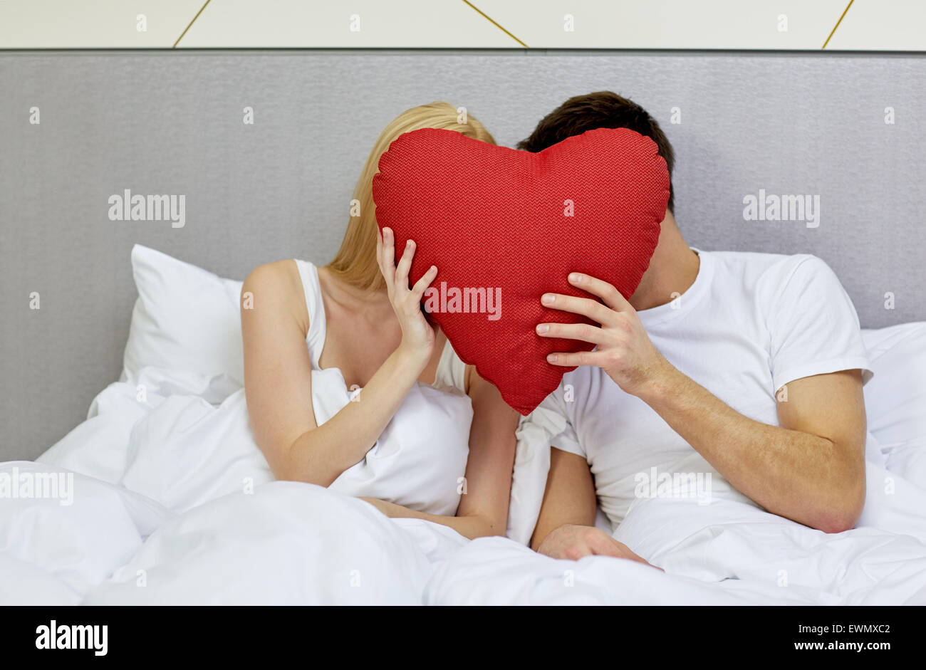 Couple heureux au lit avec oreiller en forme de coeur rouge Banque D'Images