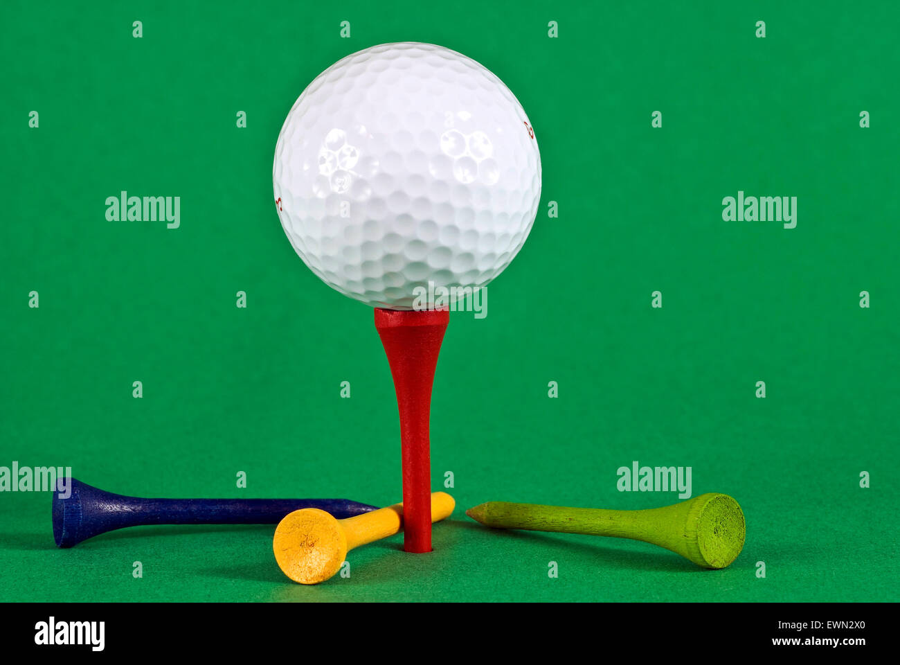Blanc lumineux balle de golf sur tee rouge sur fond vert avec tees colorés éparpillés. Banque D'Images