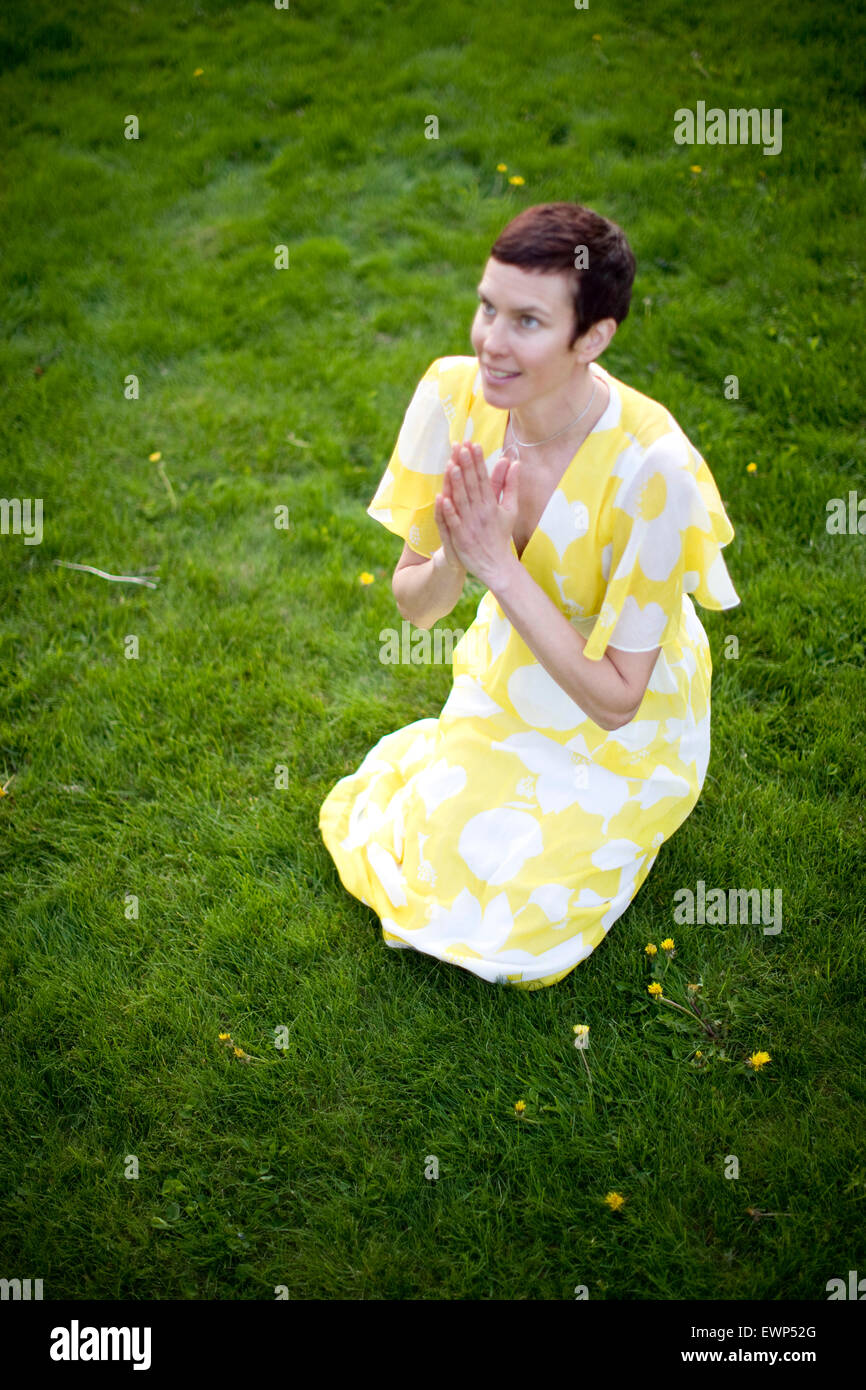 Femme adulte robe jaune en priant à l'extérieur dans sa cour avant Banque D'Images