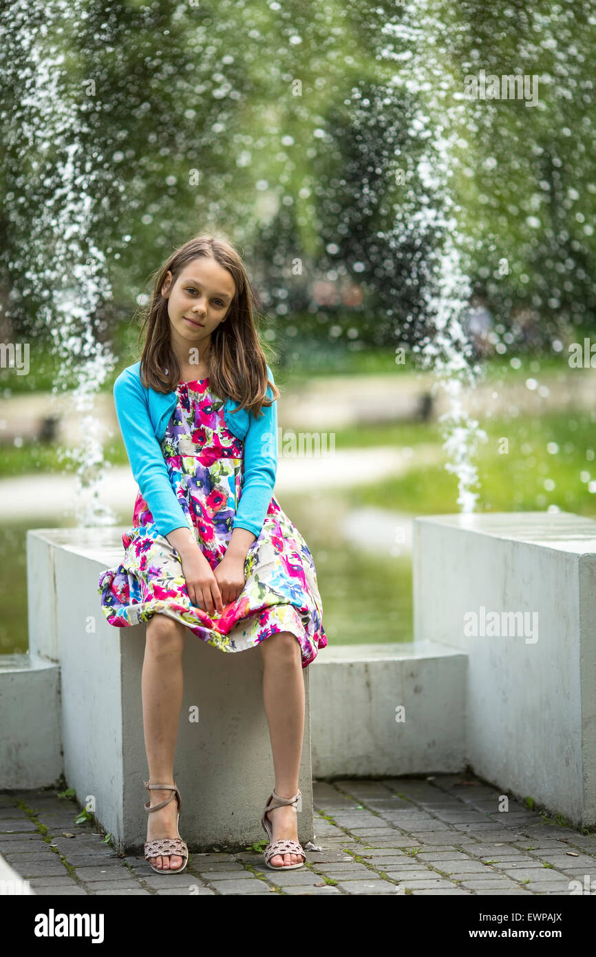 Jolie petite fille assise près de la fontaine. Banque D'Images