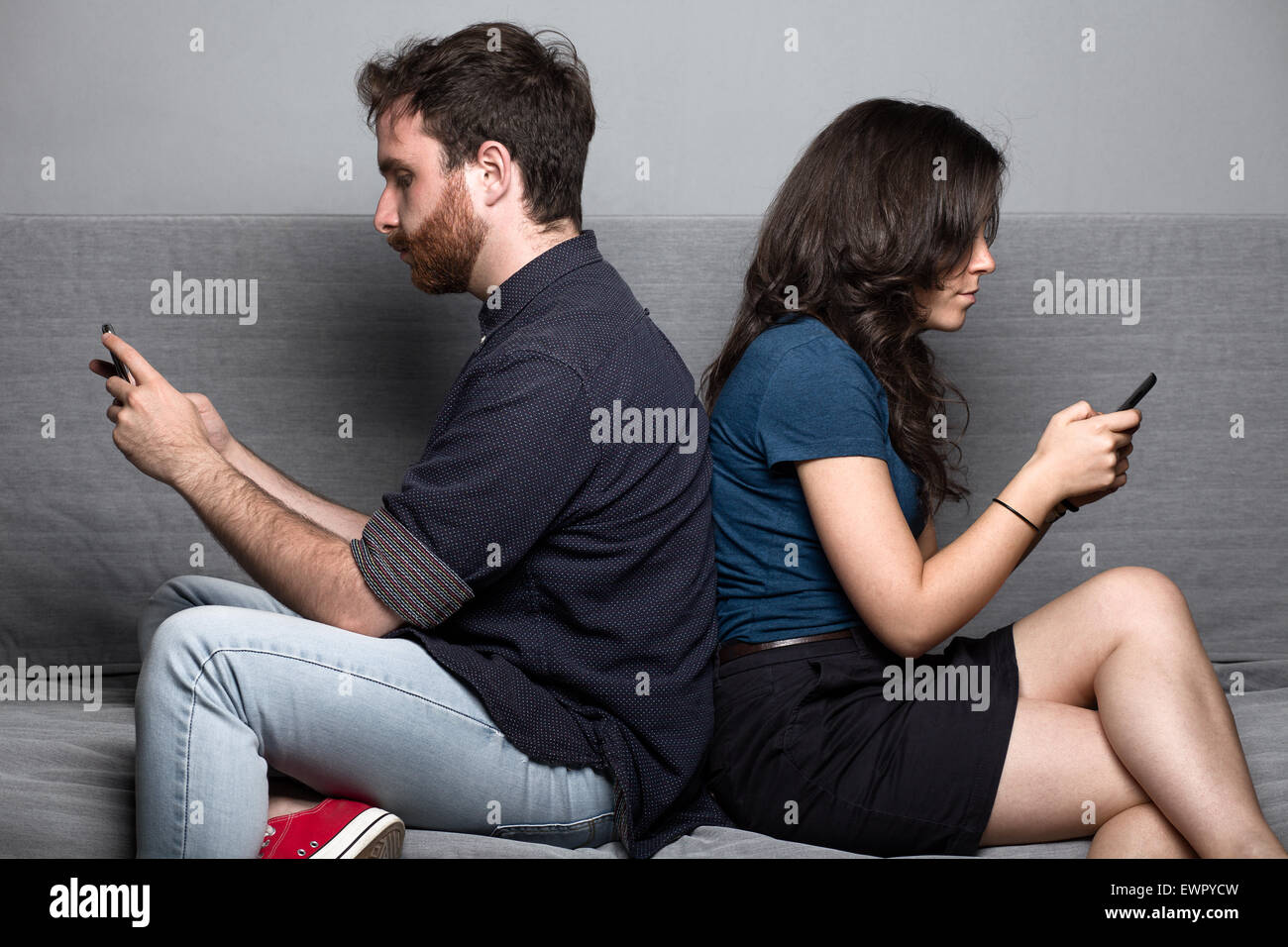 Jeune couple silencieux avec les smartphones sitting on a Couch Banque D'Images
