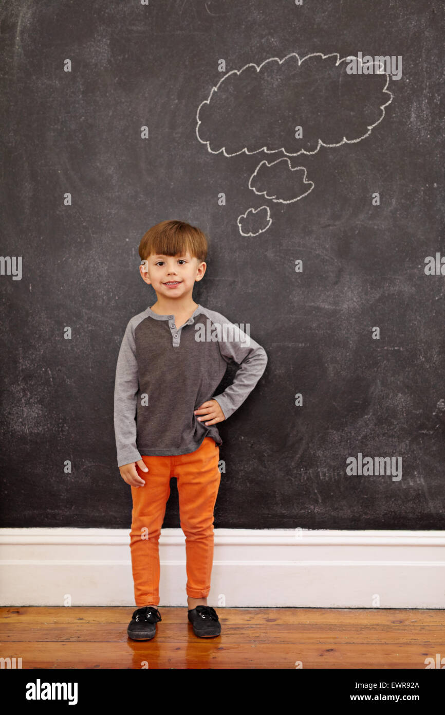 Mignon petit garçon avec une bulle de pensée sur le tableau noir. Longueur totale shot of young boy standing à la maison avec sa main sur la hanche. Banque D'Images