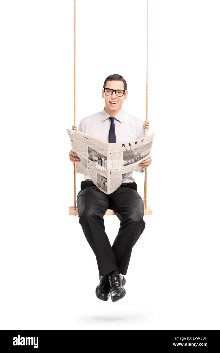 Shot vertical d'un jeune homme lisant un journal assis sur une balançoire et regardant la caméra isolé sur fond blanc Banque D'Images