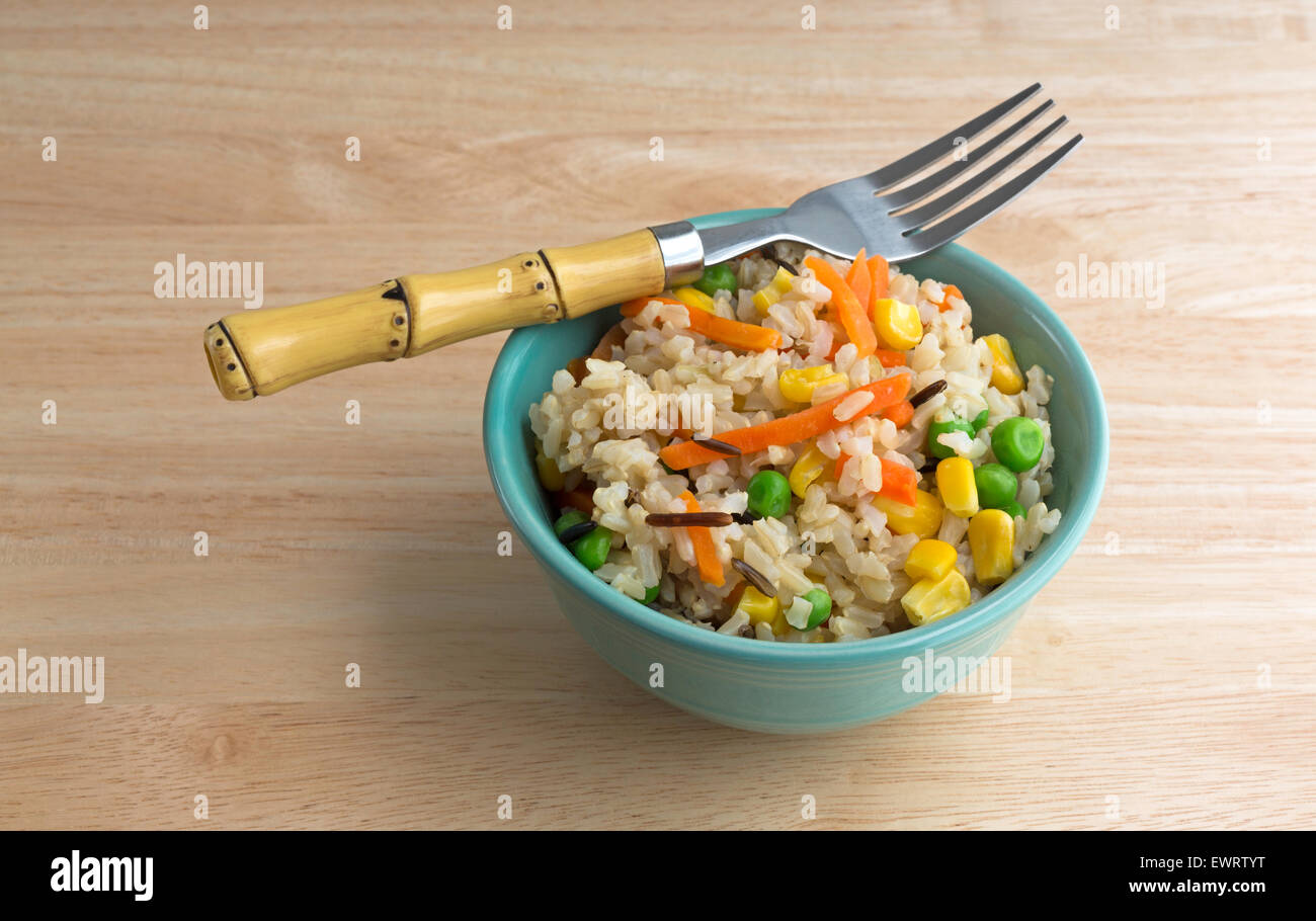 Une petite assiette de riz brun et le riz sauvage avec des petits pois, de carottes et de maïs dans un bol avec une fourchette, illuminé par la lumière naturelle. Banque D'Images