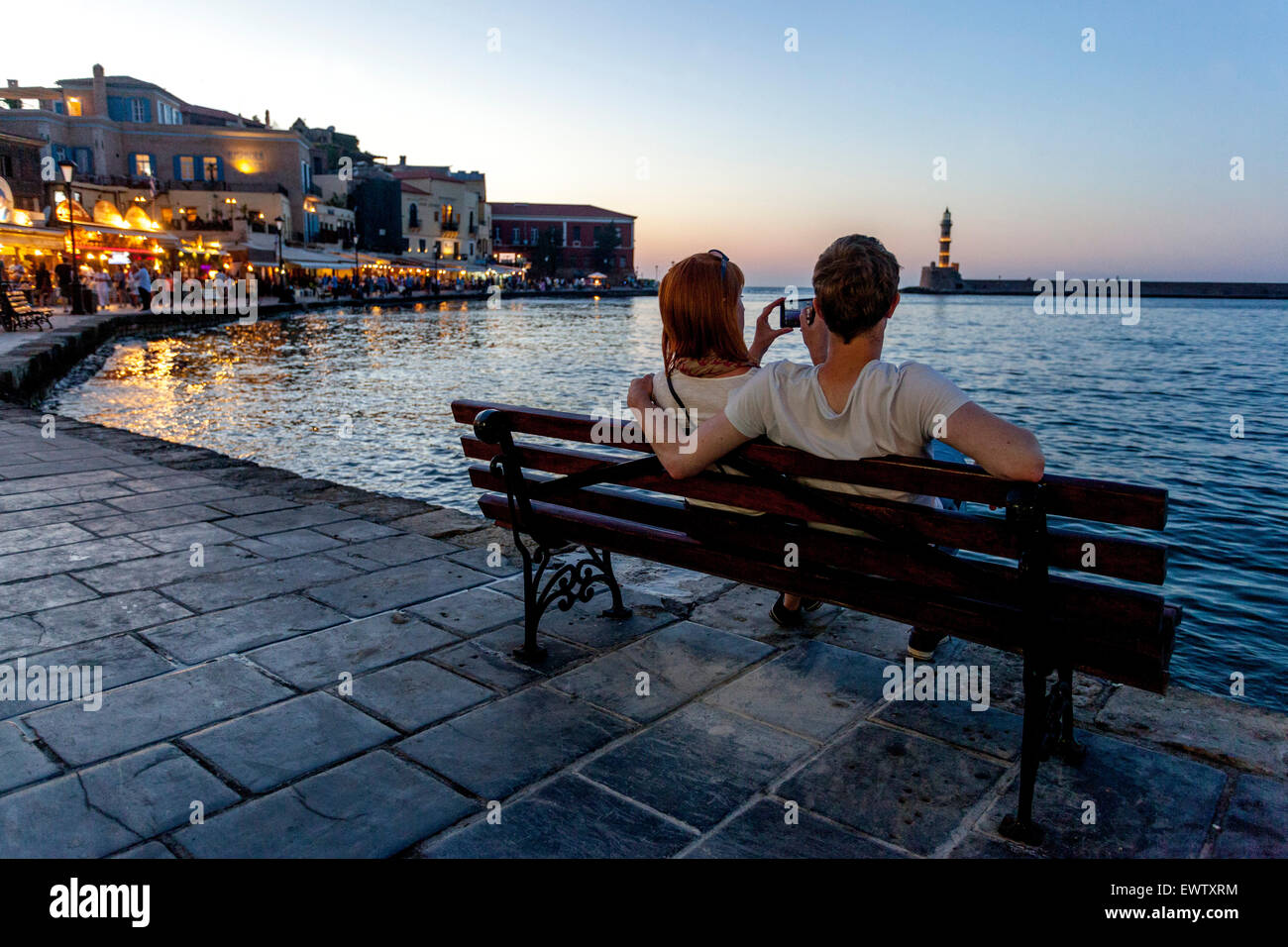 Personnes sur un banc Chania port Crète coucher de soleil Grèce été Banque D'Images