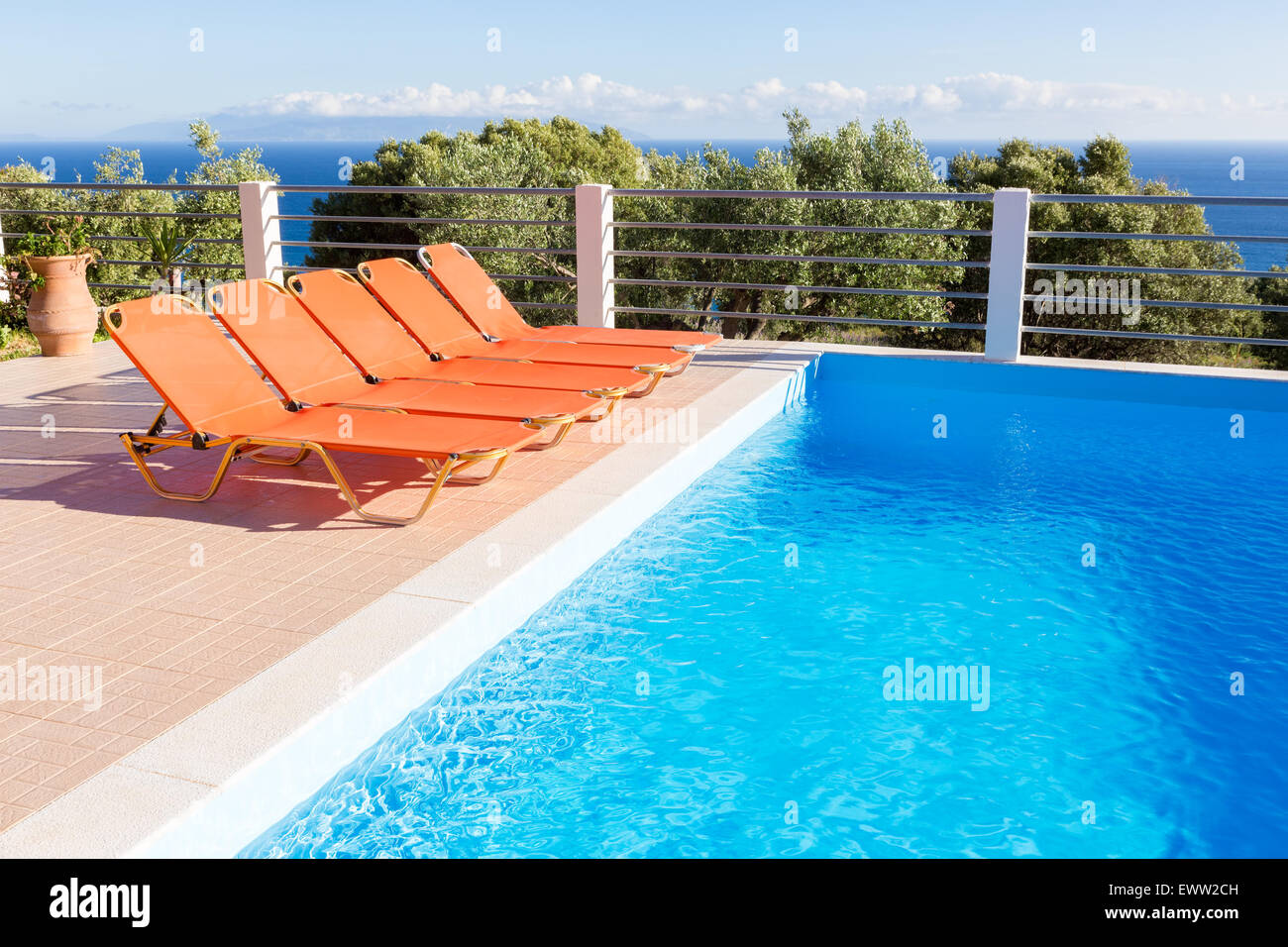Rangée de chaises longues orange pour se détendre en vacances près de piscine bleu Banque D'Images