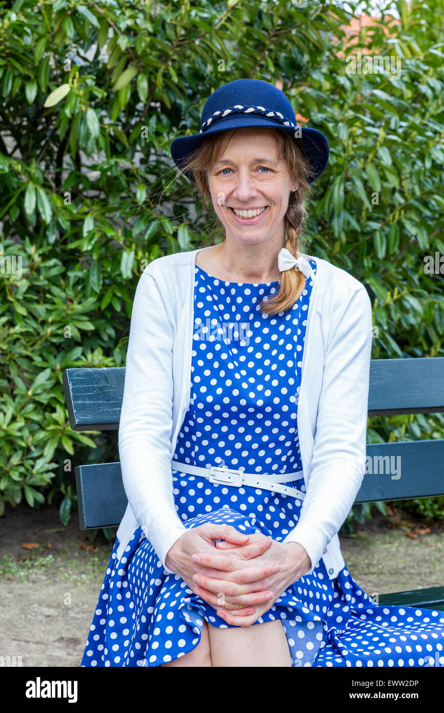Portrait femme d'âge moyen dans la région de vieux vêtements avec blue hat sitting on bench in park Banque D'Images