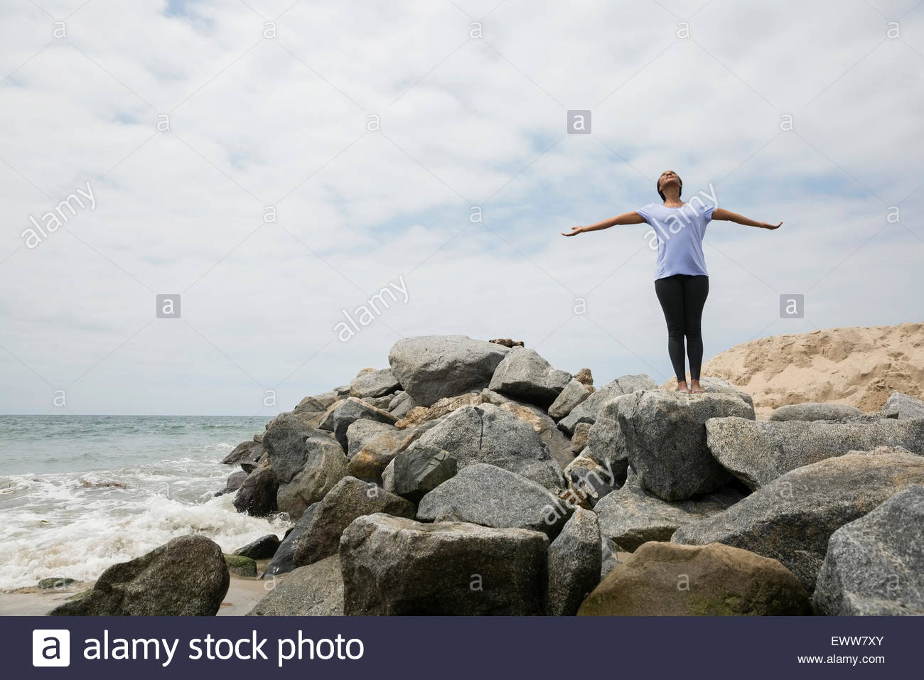 Woman doing yoga with arms outstretched beach rocks Banque D'Images