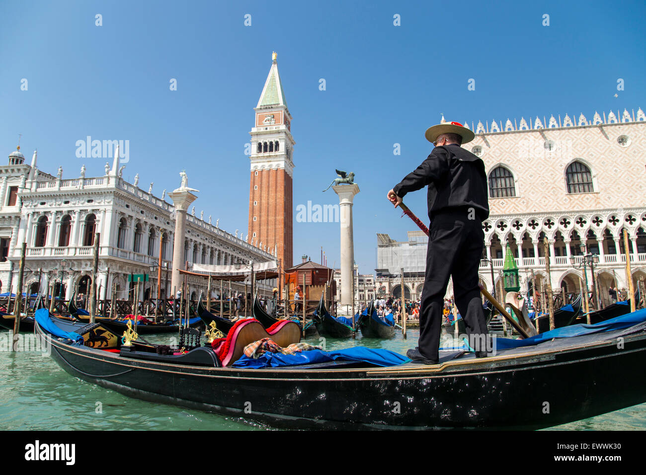 Gondolier non identifié portant un costume traditionnel dans la télécabine et naviguer sur un canal vénitien près de Campanile et du palais des Doges Banque D'Images