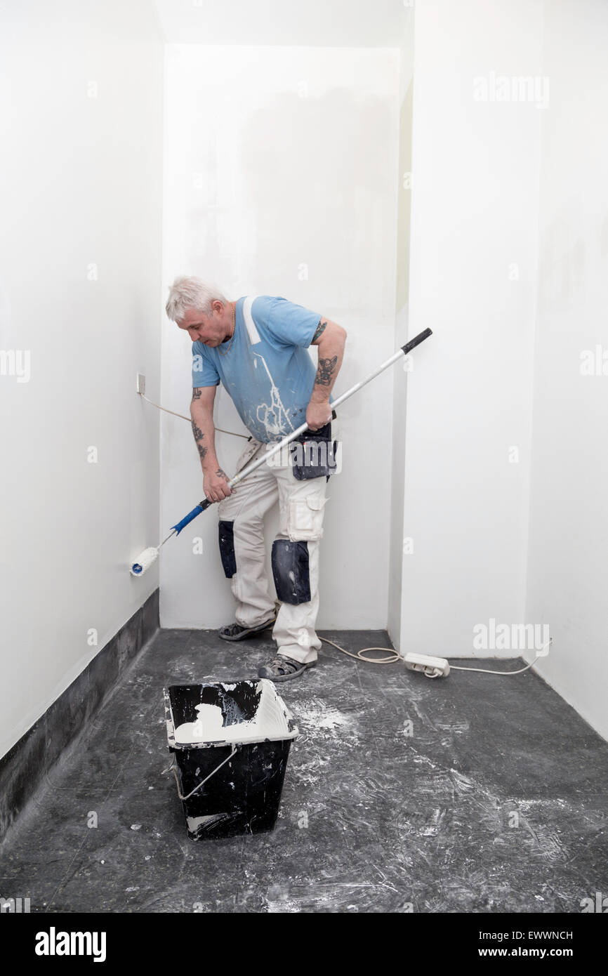 Peintre peinture des murs blanc dans une maison, seau rempli de peinture en face de lui Banque D'Images