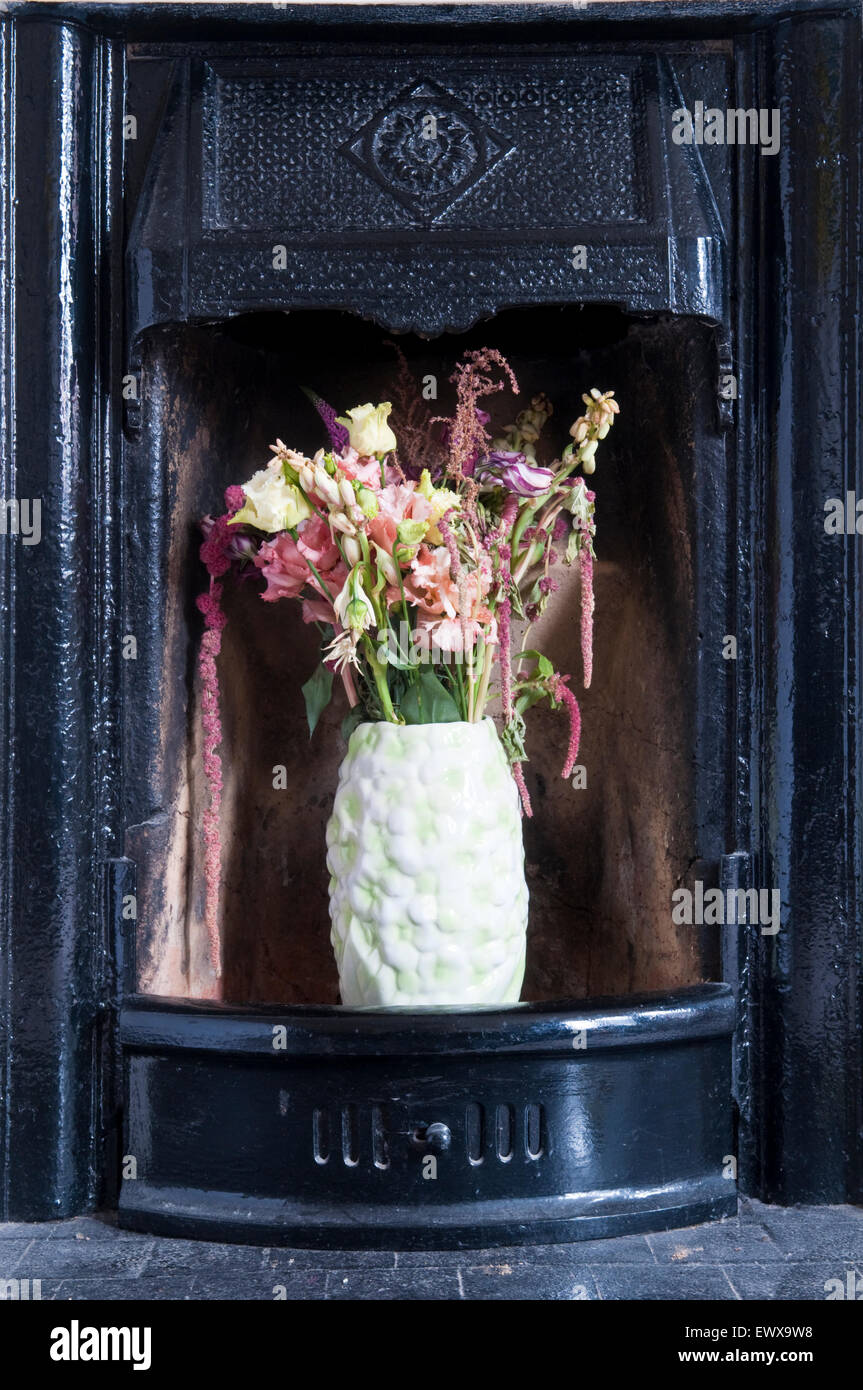 Un vase de fleurs assis dans une cheminée en fonte noire Banque D'Images