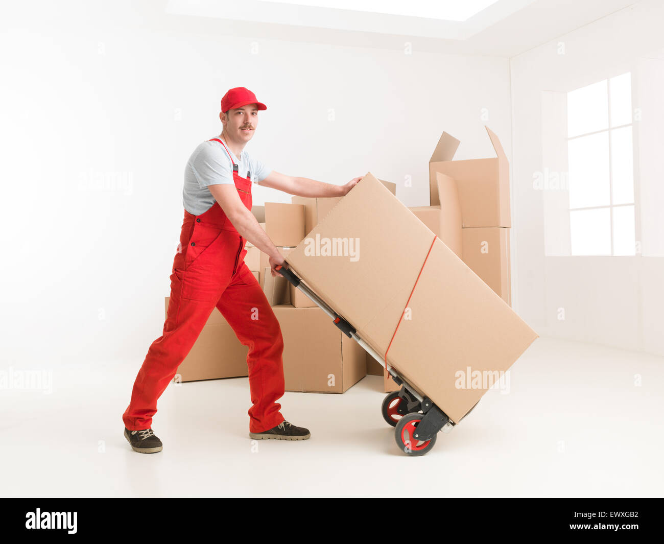 Toute la longueur de young caucasian livreur avec camion de main, le transport de boîtes de carton de déménagement. Banque D'Images