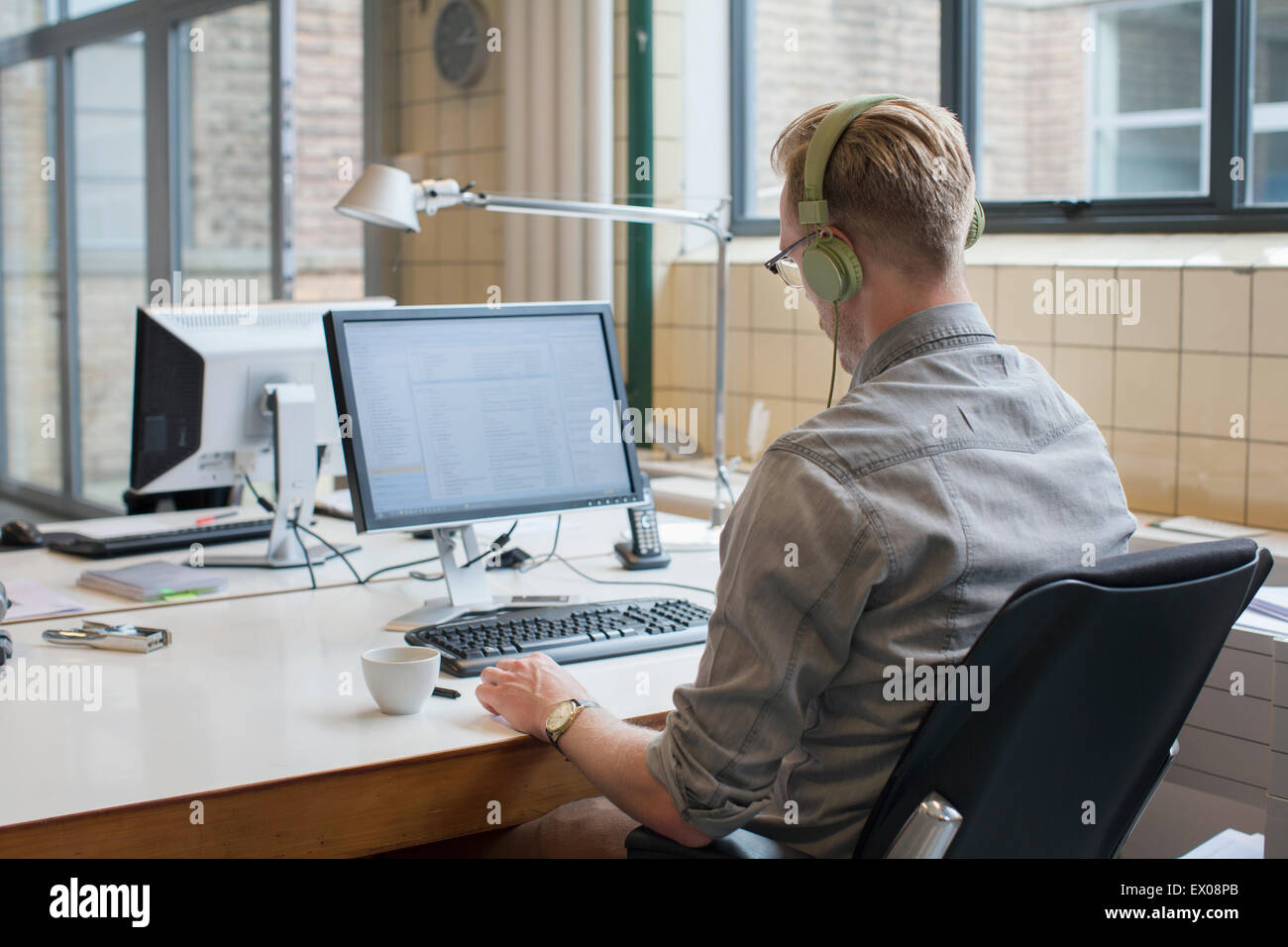 Vue arrière de l'homme à l'écoute au casque tout en travaillant à l'office de tourisme 24 Banque D'Images