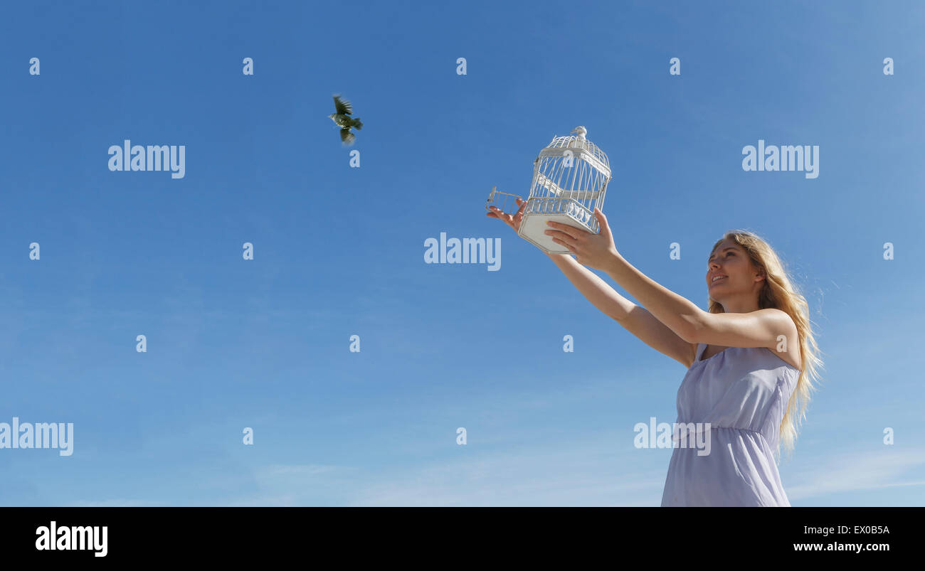 Jeune femme libérant oiseau de cage vers ciel bleu Banque D'Images