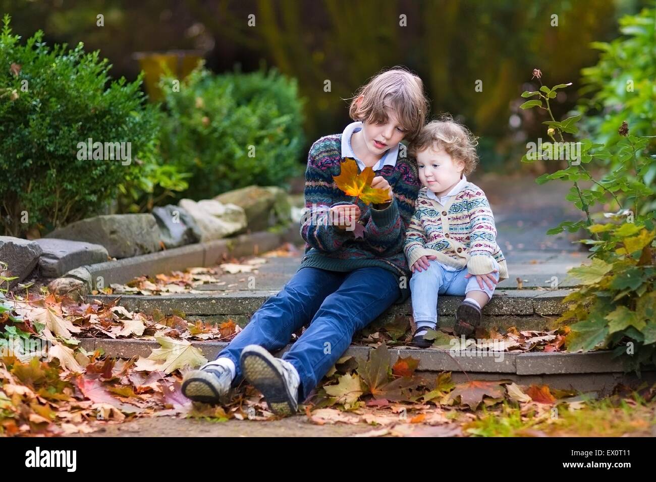 Son petit frère et petite sœur de parler et jouer avec les feuilles d'érable orange assis sur de vieux escaliers en pierre dans un parc d'automne Banque D'Images