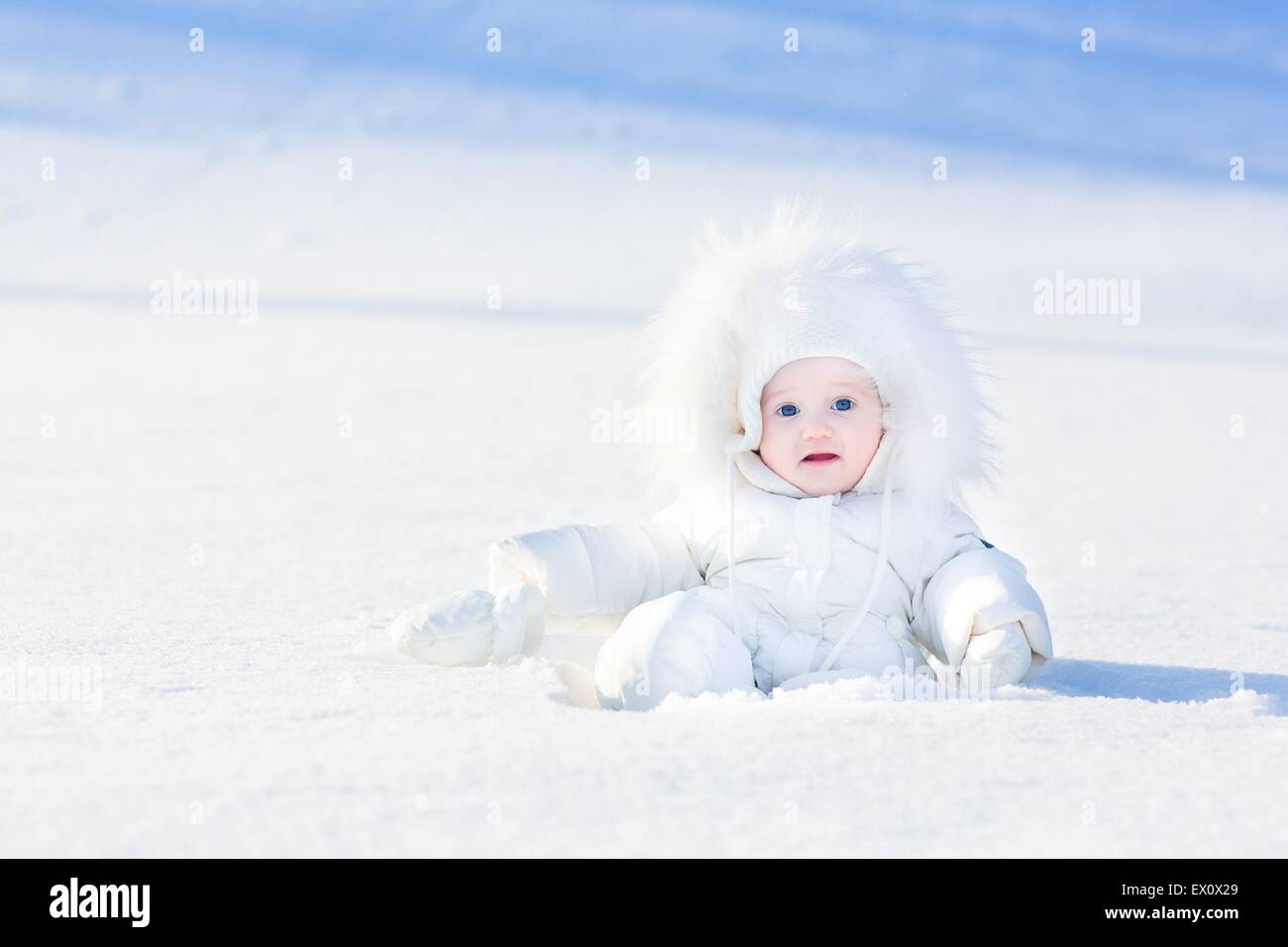 Mignon petit bébé dans une veste blanche jouent dans la neige Banque D'Images