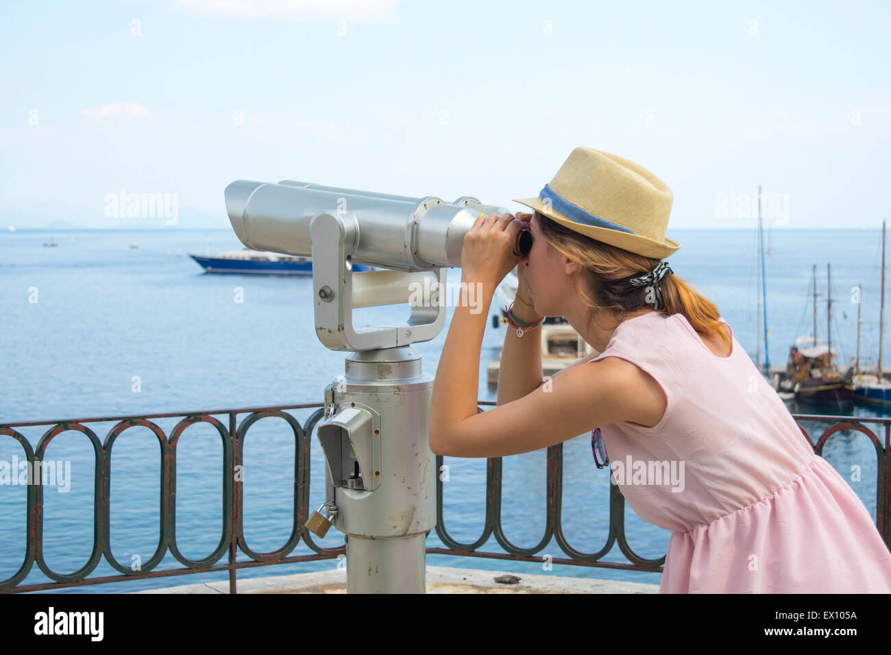 Jeune fille à la recherche publique à travers des jumelles à la mer portant chapeau de paille et robe rose Banque D'Images