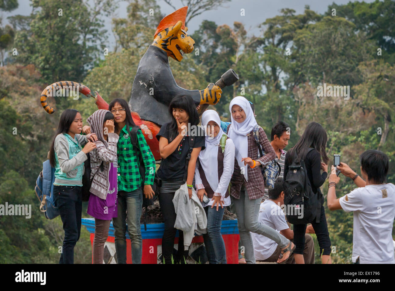 Filles d'âge scolaire ayant une séance de photo devant une statue de personnage de tigre à Padar Alam, Sumatra Sud, Indonésie. Banque D'Images
