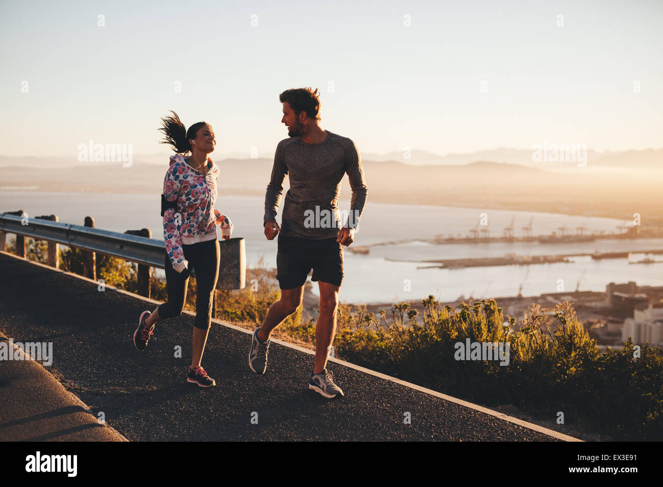 Tiré de deux personnes s'exécutant sur une route de campagne au matin. Young man and woman jogging en plein air pendant le lever du soleil. Banque D'Images