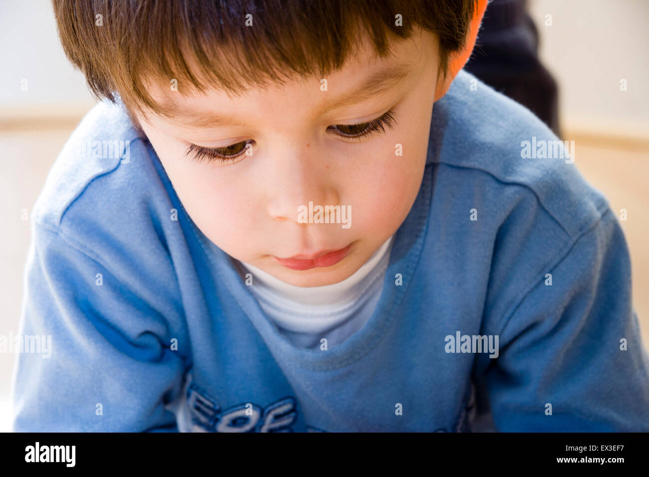 Caucasien enfant, garçon, 5-6 ans, fixant sur plancher en bois à l'intérieur et en regardant le sol. Close up of face. Expression triste. Banque D'Images