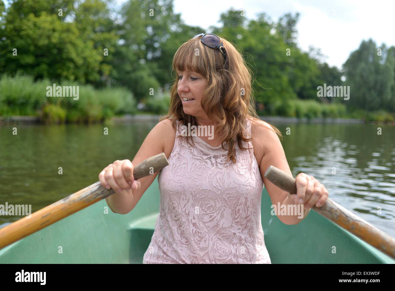 Femme attirante avirant un bateau sur un lac de canotage pendant portant une robe d'été Banque D'Images