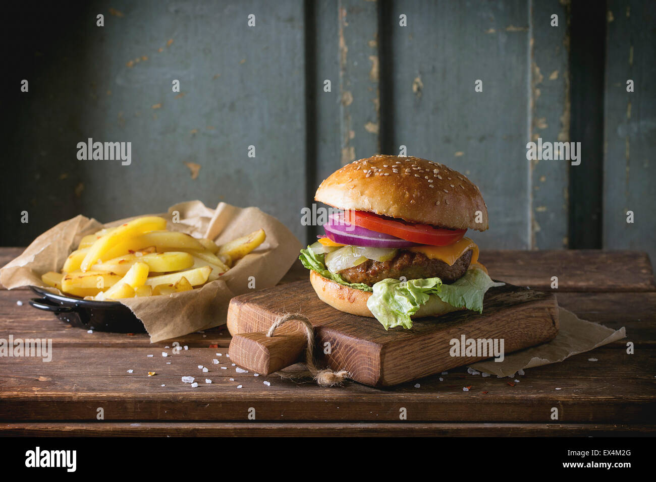 Burger maison sur petite planche à découper avec des pommes de terre, servi avec sauce ketchup et de sel de mer sur table en bois wi Banque D'Images