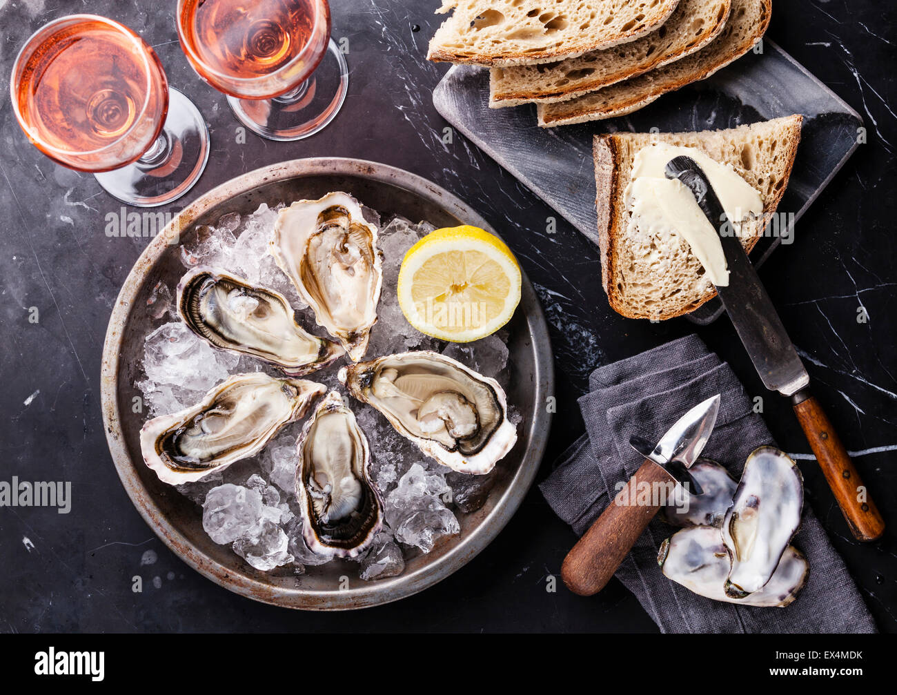 Ouvrir les huîtres sur plaque de métal avec du pain avec beurre et vin rose foncé sur fond de marbre Banque D'Images