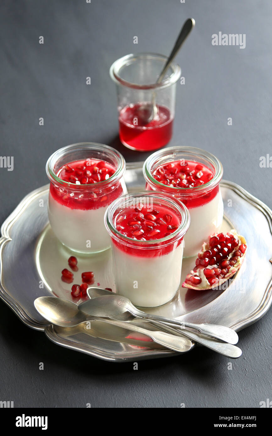 Trois pots avec le Panna Cotta sur un plateau décoré avec des graines de grenade et gelée de grenade Banque D'Images Trois pots avec le Panna Cotta sur un plateau décoré avec des graines de grenade et gelée de grenade Banque D'Images