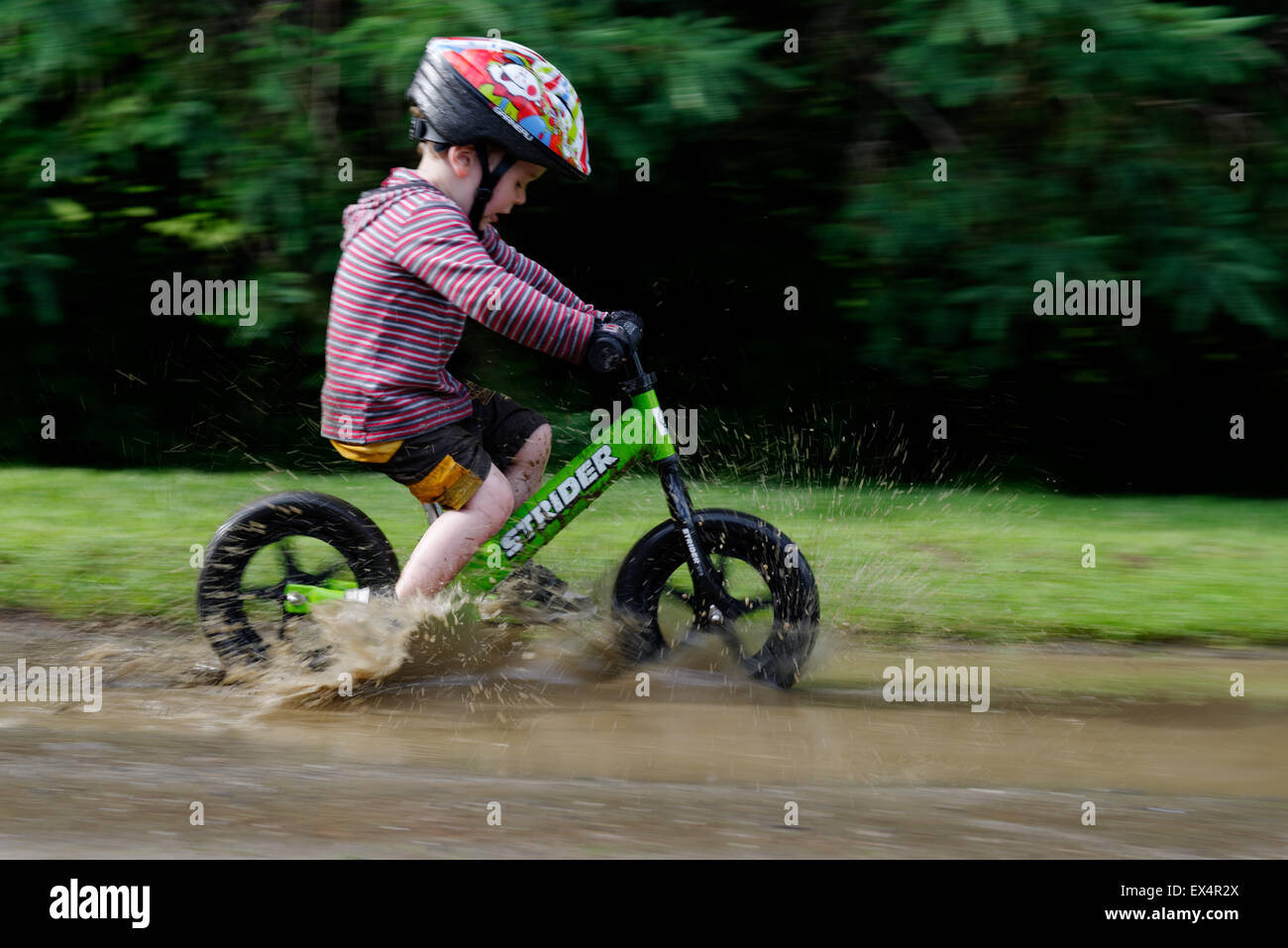 Un jeune garçon (3 ans), équitation, vélo à travers un équilibre une flaque boueuse Banque D'Images