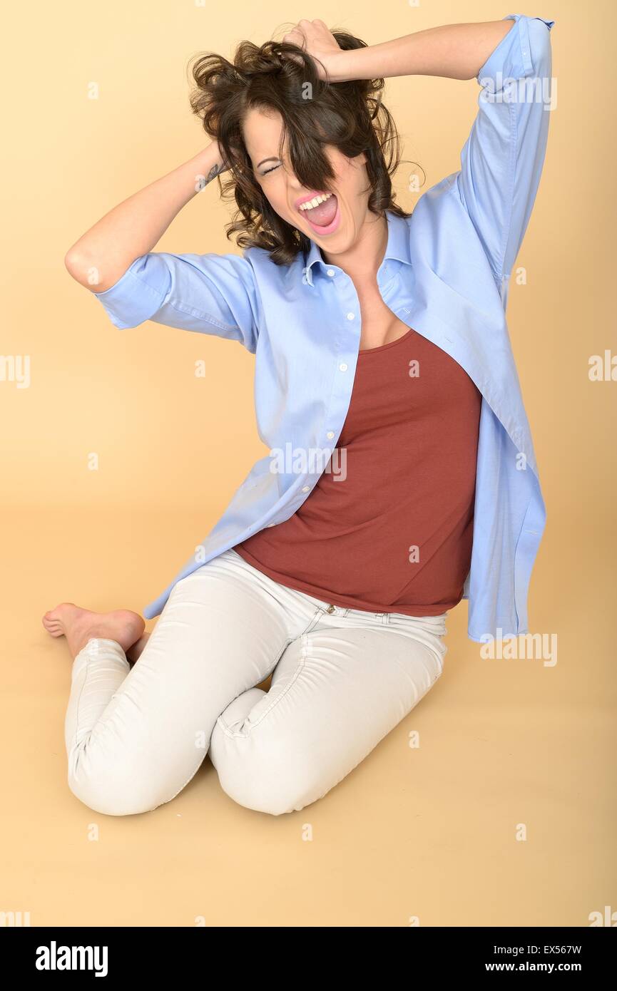 Belle jeune femme assise sur le sol portant une chemise bleu et blanc jeans avoir une crise de colère en tirant ses cheveux Banque D'Images