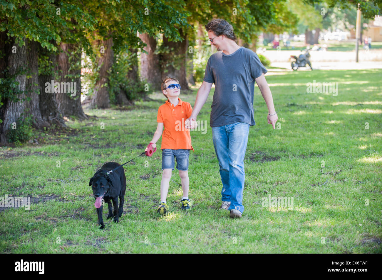 Père et fils chien labrador noir marche main dans la main ensemble Banque D'Images