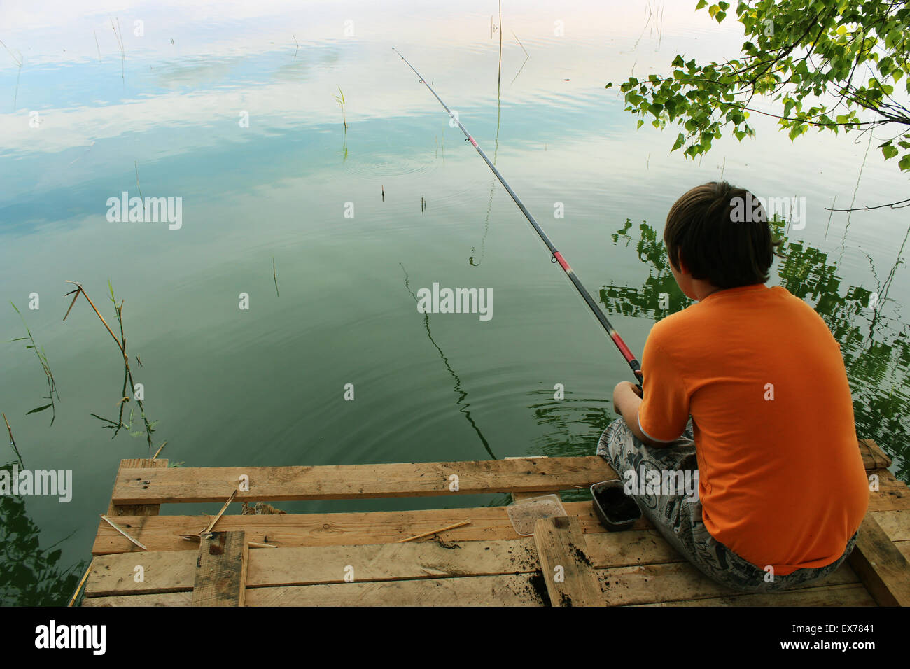 Un garçon assis sur le dock pour le poisson sur l'appât flotter sur le lac en été. Banque D'Images