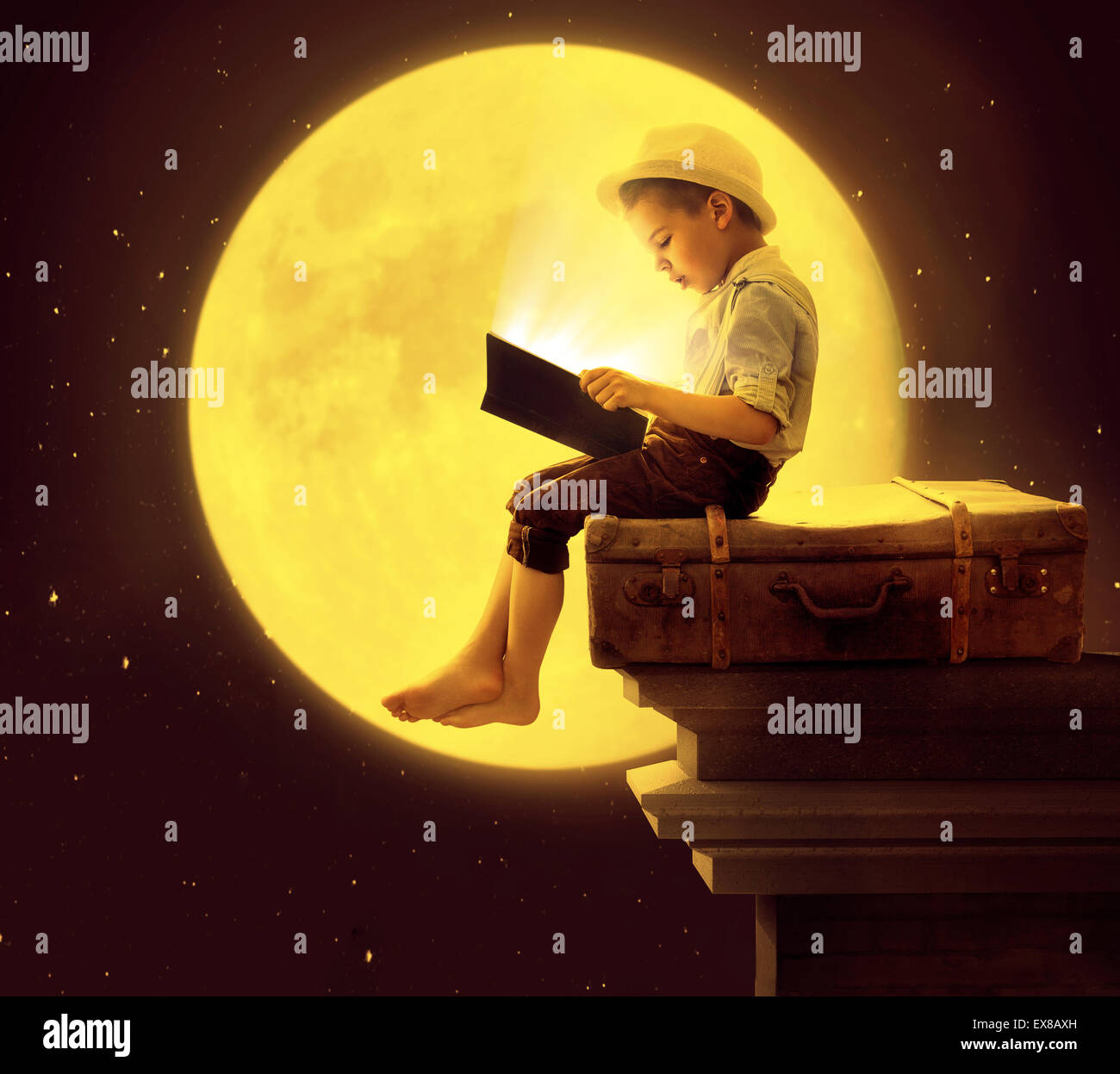 Mignon petit enfant lire un livre dans la lumière de la lune Banque D'Images