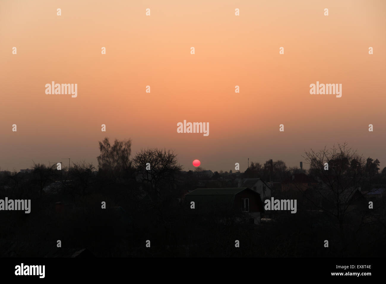 Le soleil s'assoit dans la ville plus de toits des maisons sombres Banque D'Images