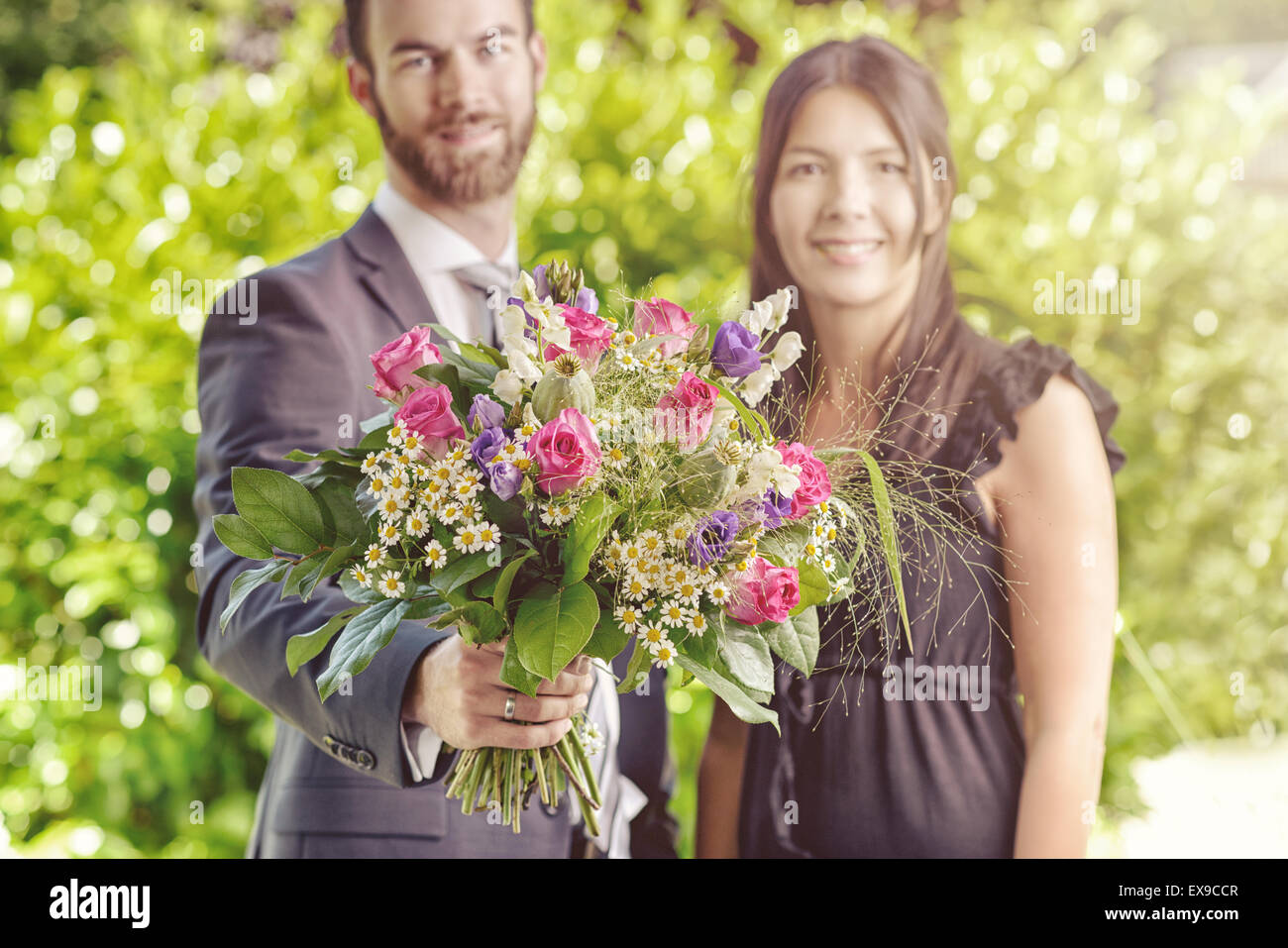 Happy Young Couple at le jardin avec bouquet de fleurs frais, souriant à la caméra. Banque D'Images