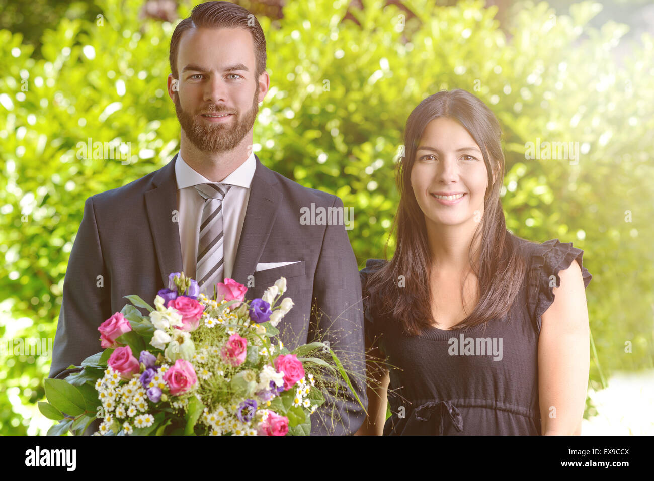 Happy Young Couple at le jardin avec bouquet de fleurs frais, souriant à la caméra. Banque D'Images